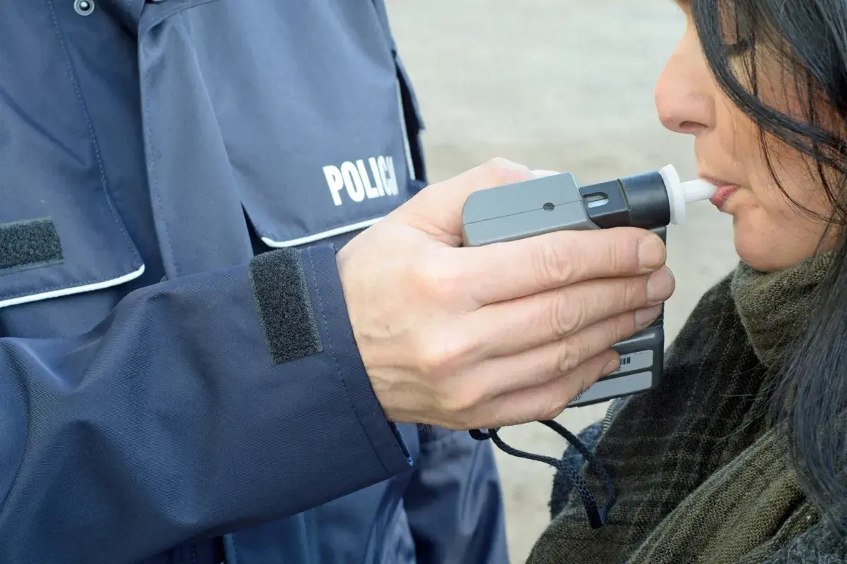 Policjant w mundurze z napisem "POLICJA" trzyma alkomat, a kobieta dmucha w jego ustnik. To przykład, jak dmuchać w alkomat.