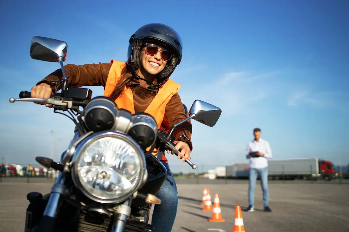 Uśmiechnięta kursantka na motorze, w kamizelce odblaskowej i kasku, uczy się jeździć. Zastanawiasz się, ile kosztuje prawo jazdy na motor?