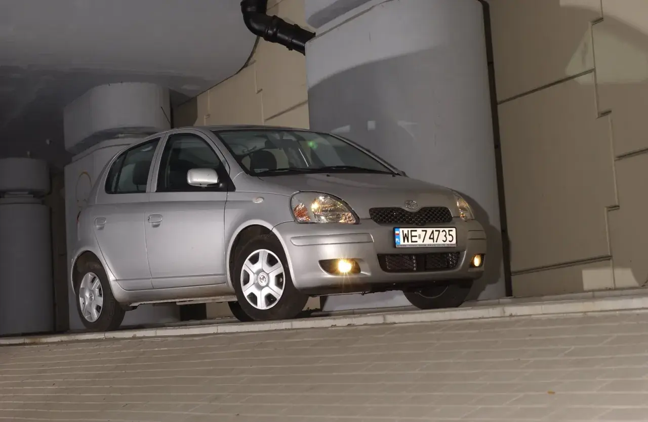 Srebrny Toyota Yaris 1.4 D4D, z tablicą WE 74735, zaparkowany pod betonowym zadaszeniem.