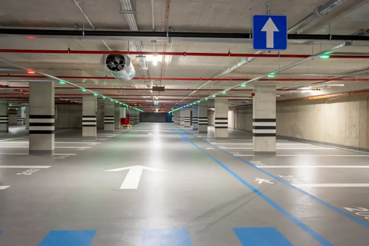 Pusta hala garażowa z wyznaczonymi miejscami parkingowymi i strzałkami na podłodze. Idealne miejsce, gdzie można poćwiczyć jazdę samochodem w Warszawie.