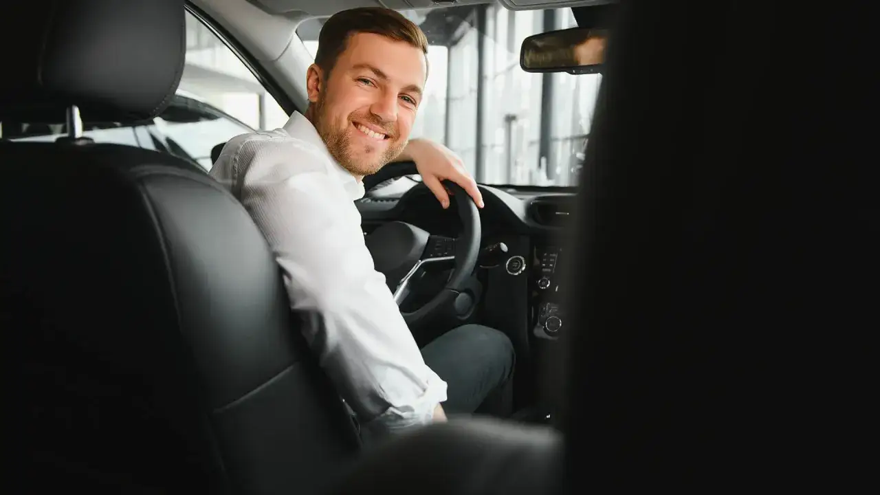 Uśmiechnięty mężczyzna za kierownicą, gotowy do pracy. Dowiedz się, jak zostać kierowcą Opti Taxi i zacznij zarabiać!