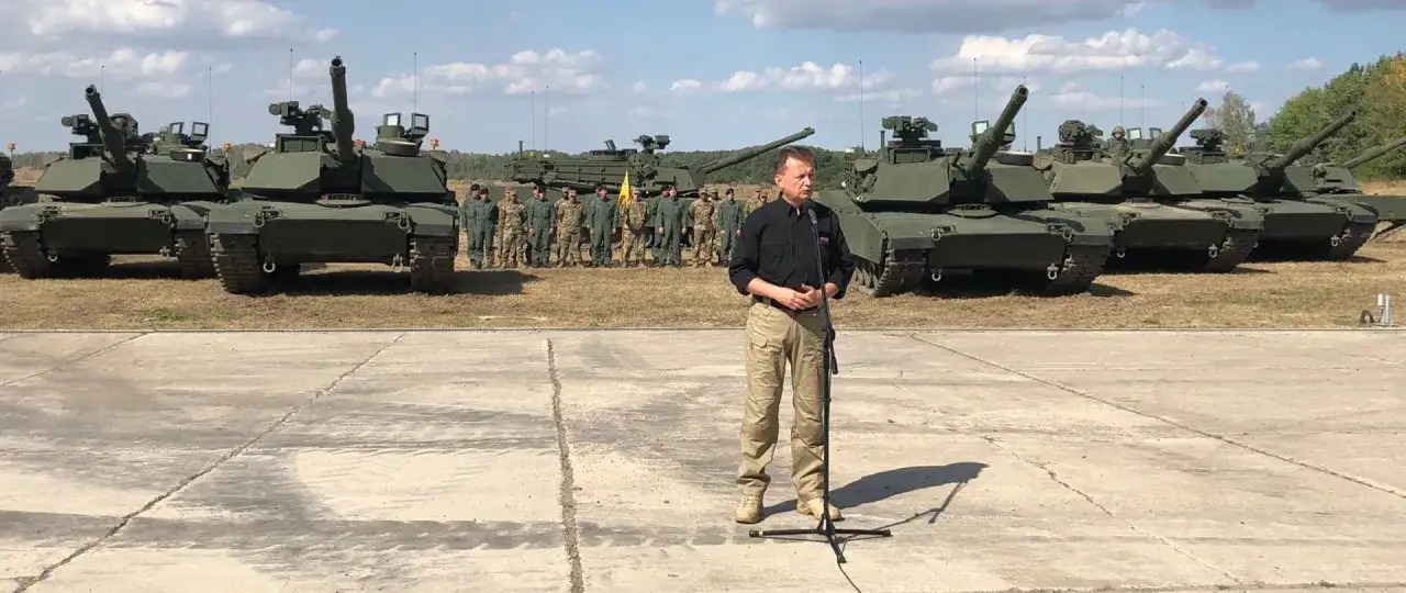 Mężczyzna przemawia przed rzędem czołg&oacute;w, być może wyjaśniając, jak zostać kierowcą czołgu.