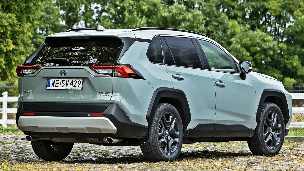 Szary Toyota RAV4 Hybrid AWD na tle drzew. Zastanawiasz się nad pojemnością baku? Ten model oferuje świetny zasięg.
