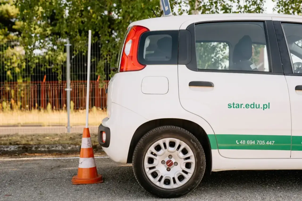 Biały samochód szkoleniowy z pachołkiem obok. Zastanawiasz się, ile kosztuje prawo jazdy? Sprawdź ofertę na star.edu.pl.