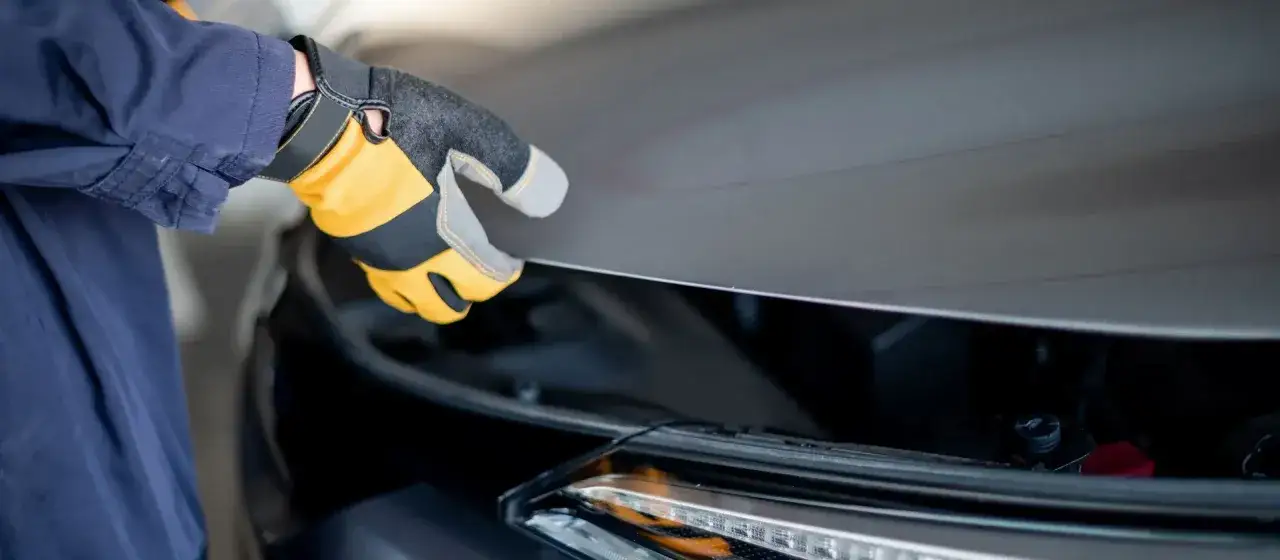 Ręka w rękawicy zamyka maskę samochodu. Co jeśli samochód nie przejdzie przeglądu? Czas na wizytę u mechanika.