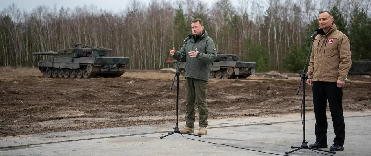 Dw&oacute;ch mężczyzn przemawia na tle czołg&oacute;w Leopard. Dowiedz się, jak zostać kierowcą czołgu i dołączyć do wojska.