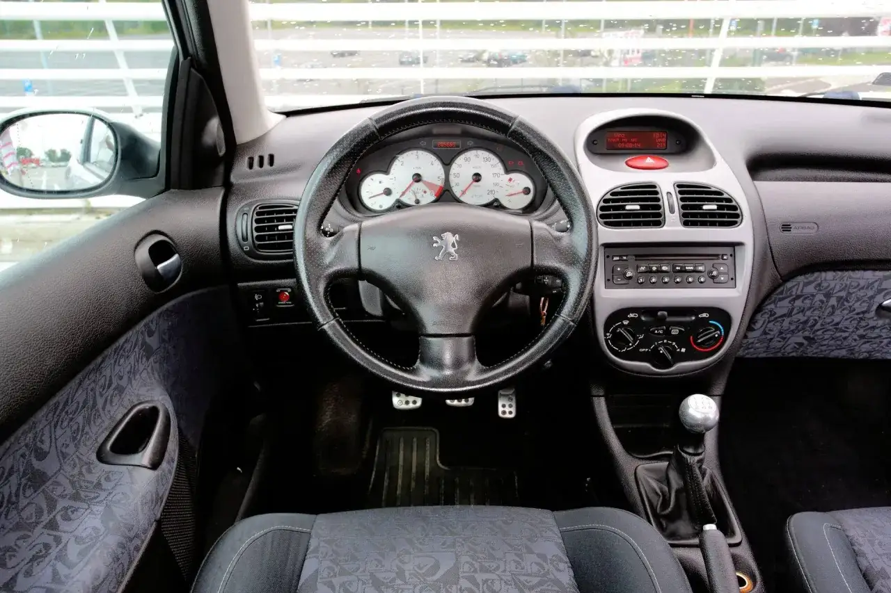 Wnętrze Peugeot 206 1.4 HDI. Na desce rozdzielczej wskaźniki, radio, nawiewy. Kierowca zastanawia się nad pojemnością baku.