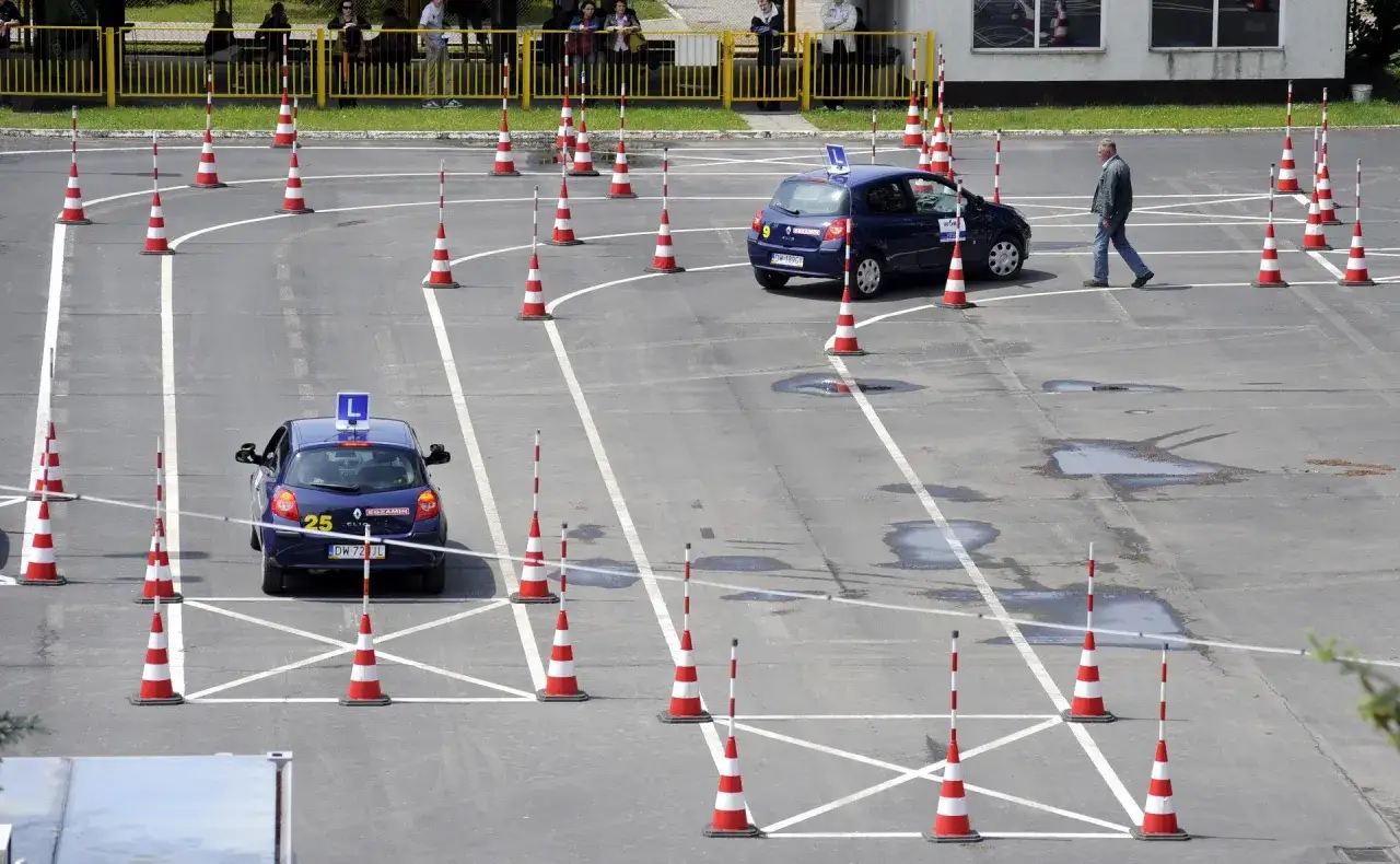Tor przeszkód na placu manewrowym, gdzie kursanci uczą się, jak zdać egzamin na prawo jazdy. Dwa samochody z literą