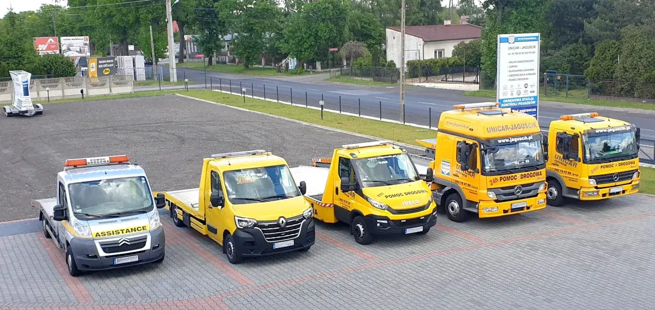 Flota pojazdów pomocy drogowej, w tym jeden srebrny z napisem ASSISTANCE, gotowa do zapewnienia ubezpieczenie assistance.