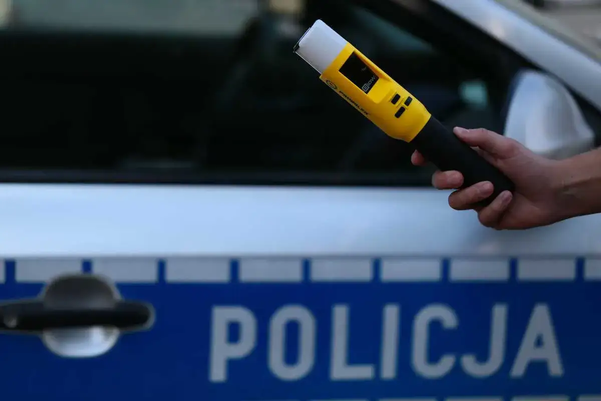 Dłoń trzyma ż&oacute;łty alkomat przed radiowozem. Czy można odm&oacute;wić badania alkomatem?