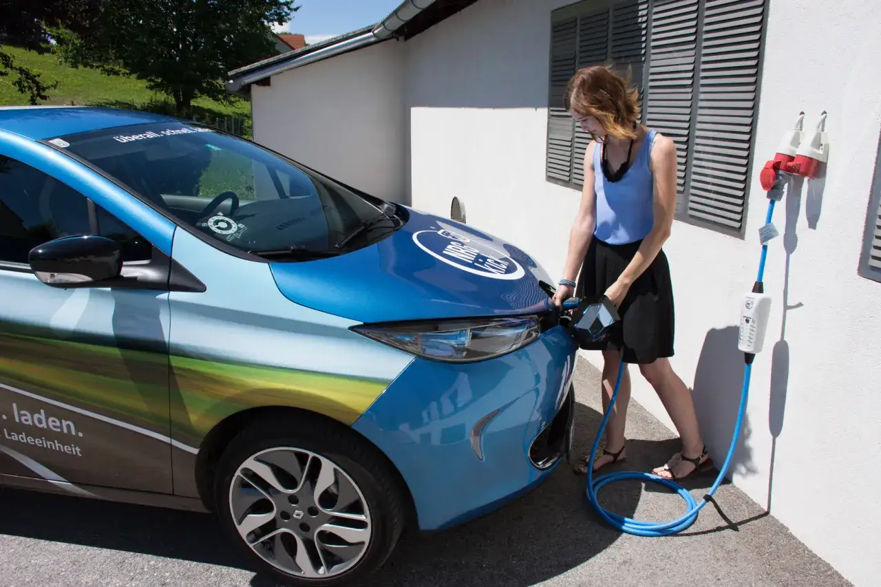 Kobieta ładuje niebieski samoch&oacute;d elektryczny. Zastanawiasz się, ile kosztuje ładowanie samochodu elektrycznego?