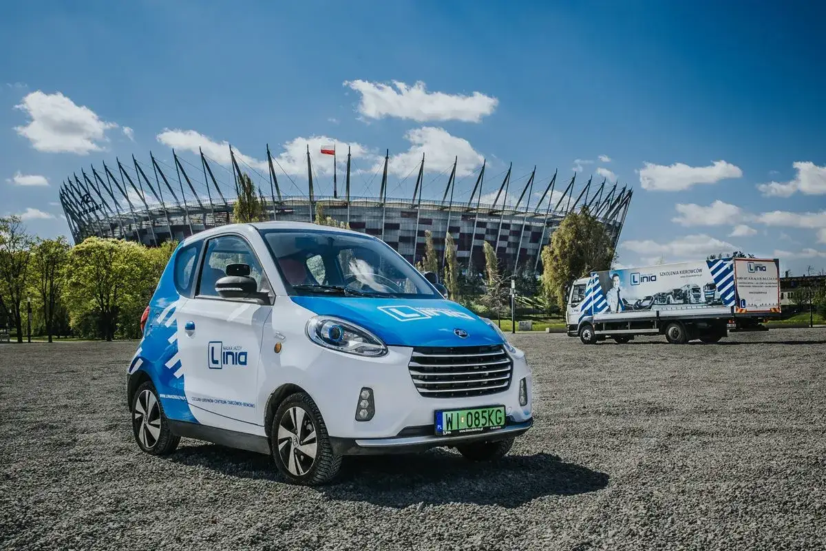 Mały samochód elektryczny i ciężarówka szkoleniowa przed stadionem. Prawo jazdy kat B1 czym można jeździć? Takimi pojazdami!