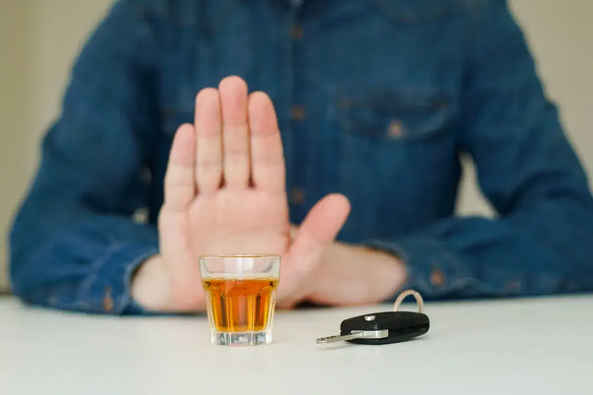 Dłoń zatrzymuje kieliszek z alkoholem, obok kluczyki do auta. Pamiętaj, że na ile zabierają prawo jazdy za alkohol 1 promil, to już za dużo!