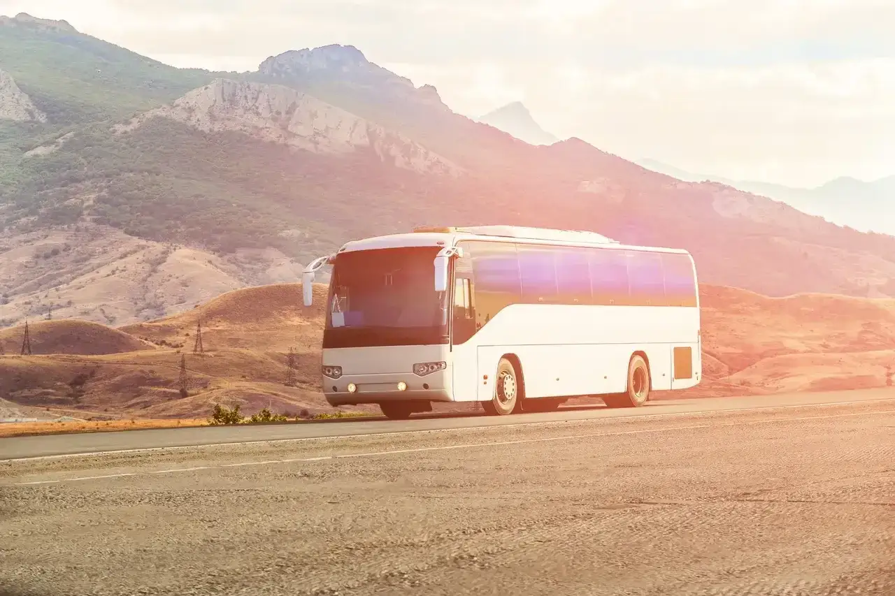 Biały autokar jedzie drogą wśród gór. Zastanawiasz się, ile zarabia kierowca autobusu?
