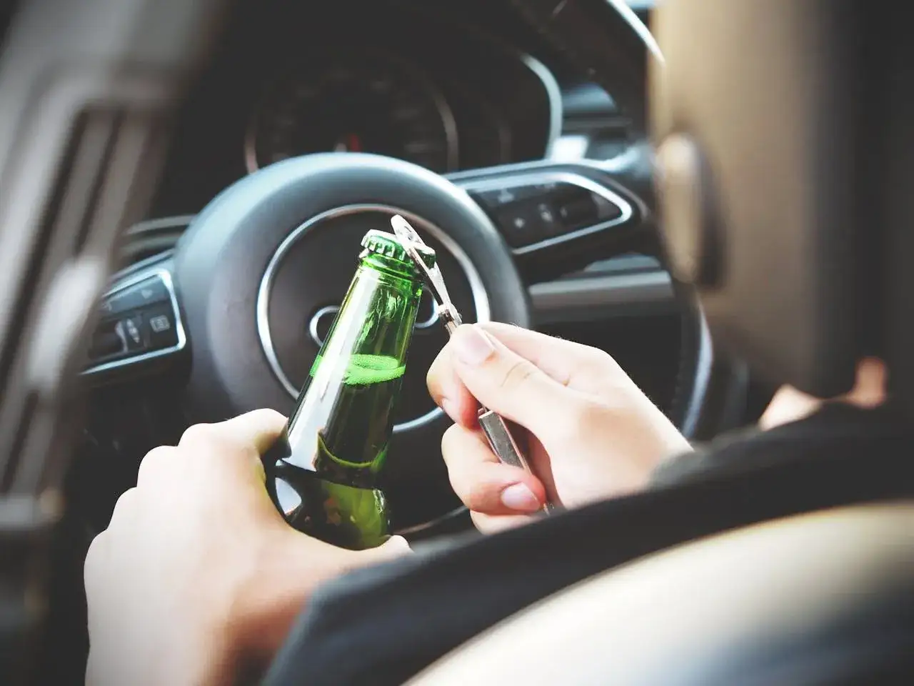 Kierowca otwiera piwo za kierownicą. Pamiętaj, że na ile zabierają prawo jazdy za alkohol 1 promil, to nie warto ryzykować.