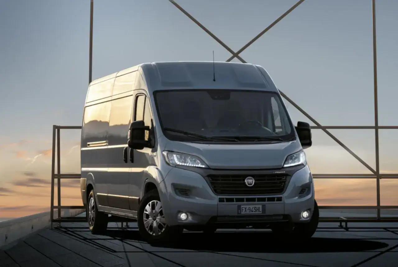 Szary Fiat Ducato na tle zachodzącego słońca. Zastanawiasz się nad pojemnością baku? Ten model oferuje duży zasięg.