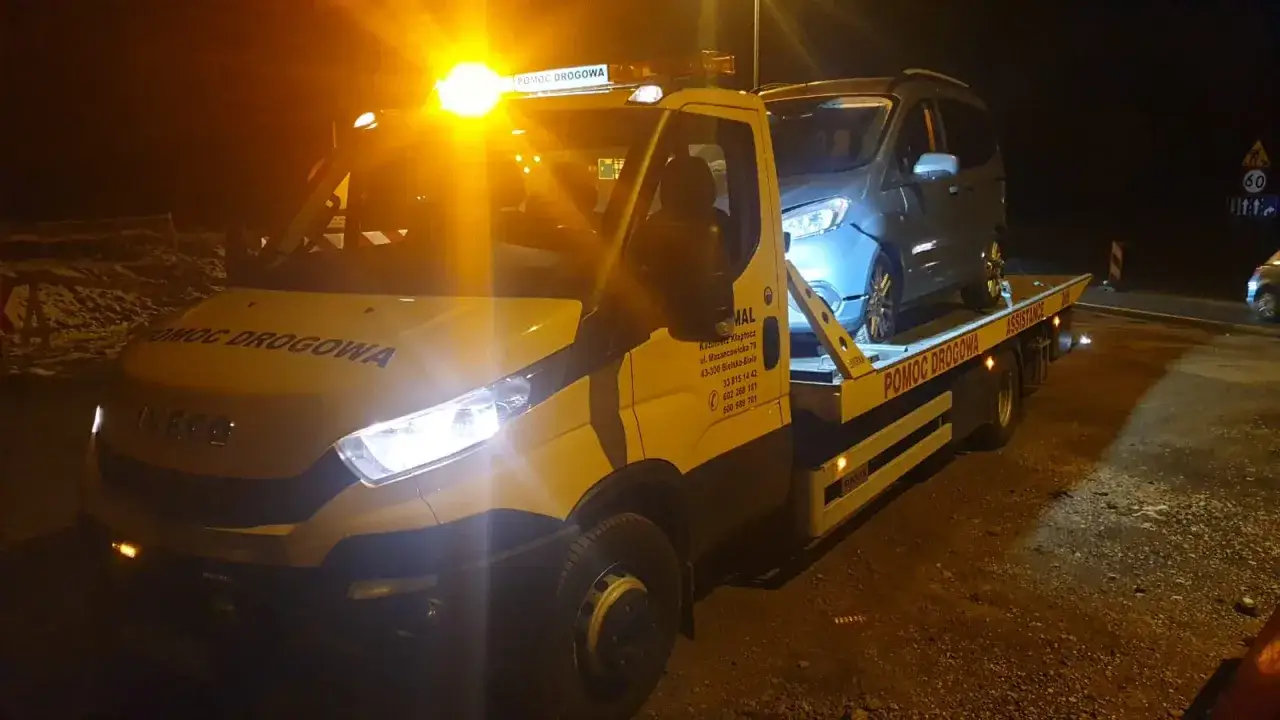 Pomoc drogowa Iveco z platformą transportuje samochód. Pomarańczowe światła ostrzegawcze są włączone. Ergo Hestia assistance czuwa nad bezpieczeństwem.
