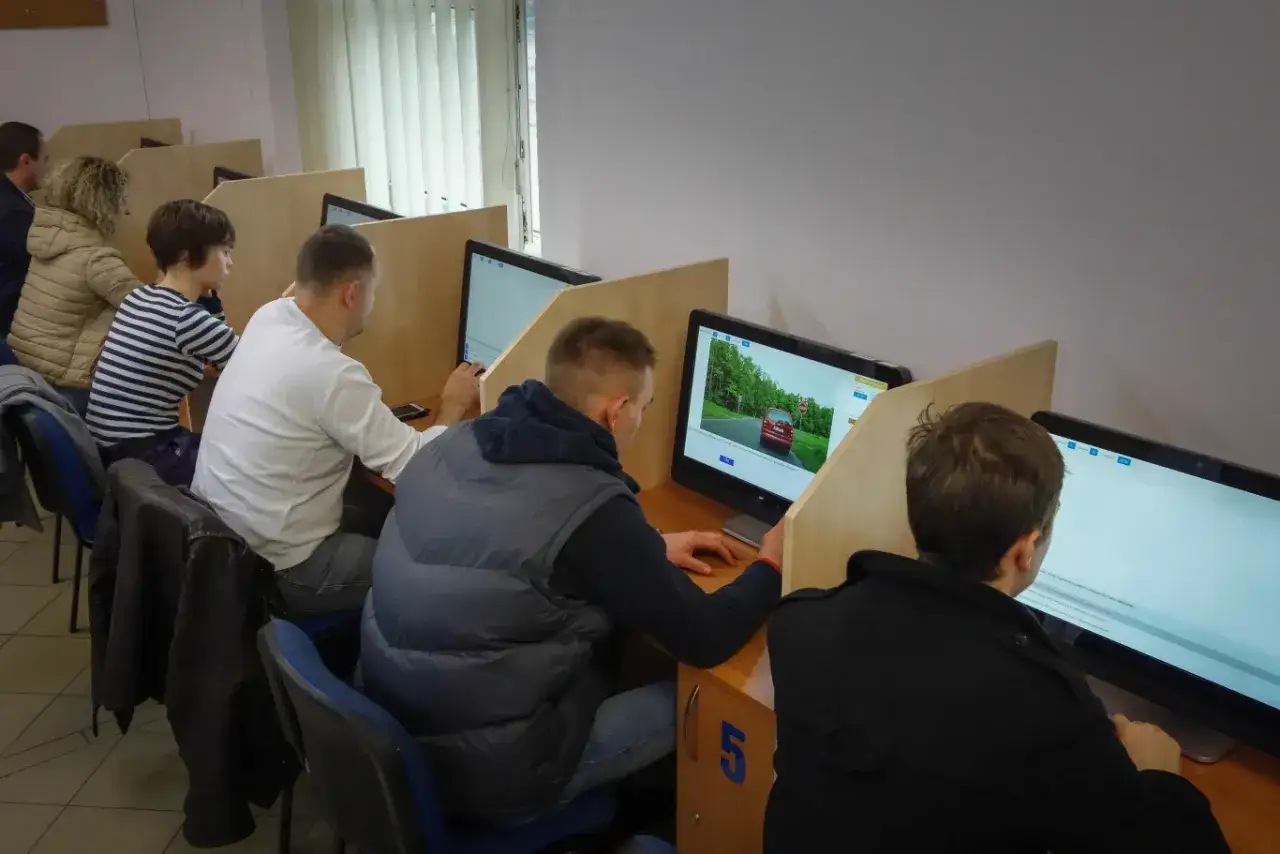Ludzie siedzą przy komputerach, rozwiązując testy. Zastanawiają się, ile punkt&oacute;w na egzaminie prawo jazdy zdobędą.