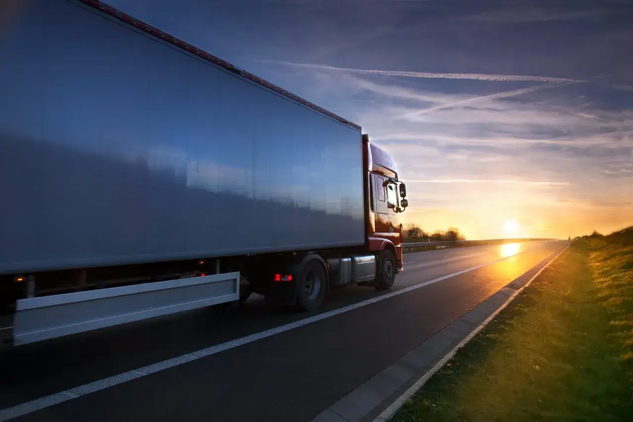 Czerwony tir pędzi autostradą o zachodzie słońca. Czy warto zostać kierowcą tira? Widoki i wolność są kuszące.