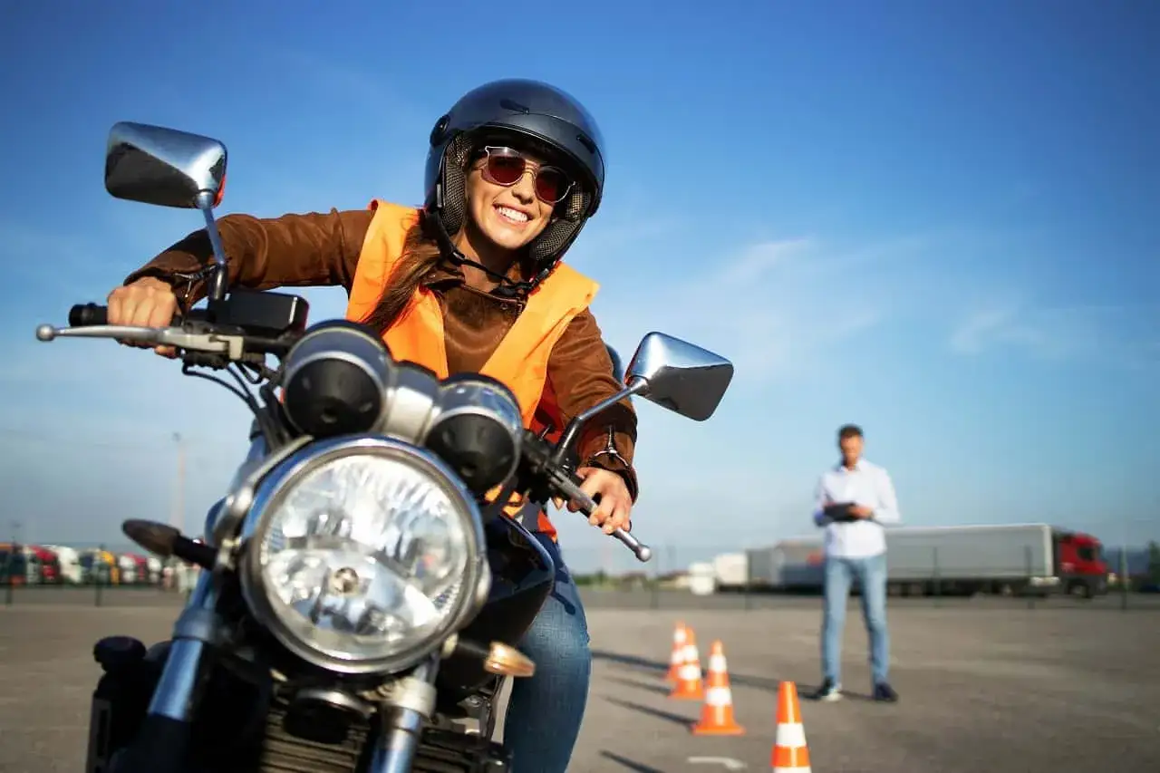 Uśmiechnięta kursantka na motorze, w kasku i kamizelce, uczy się jeździć. Zastanawiasz się, ile kosztuje prawo jazdy na motor?