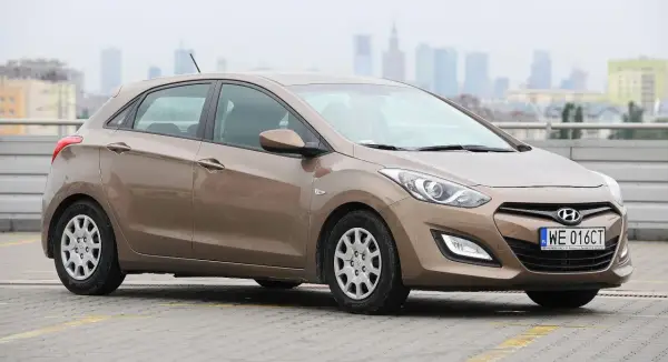 Brązowy Hyundai i30 1.4 benzyna na parkingu, w tle miejska panorama.